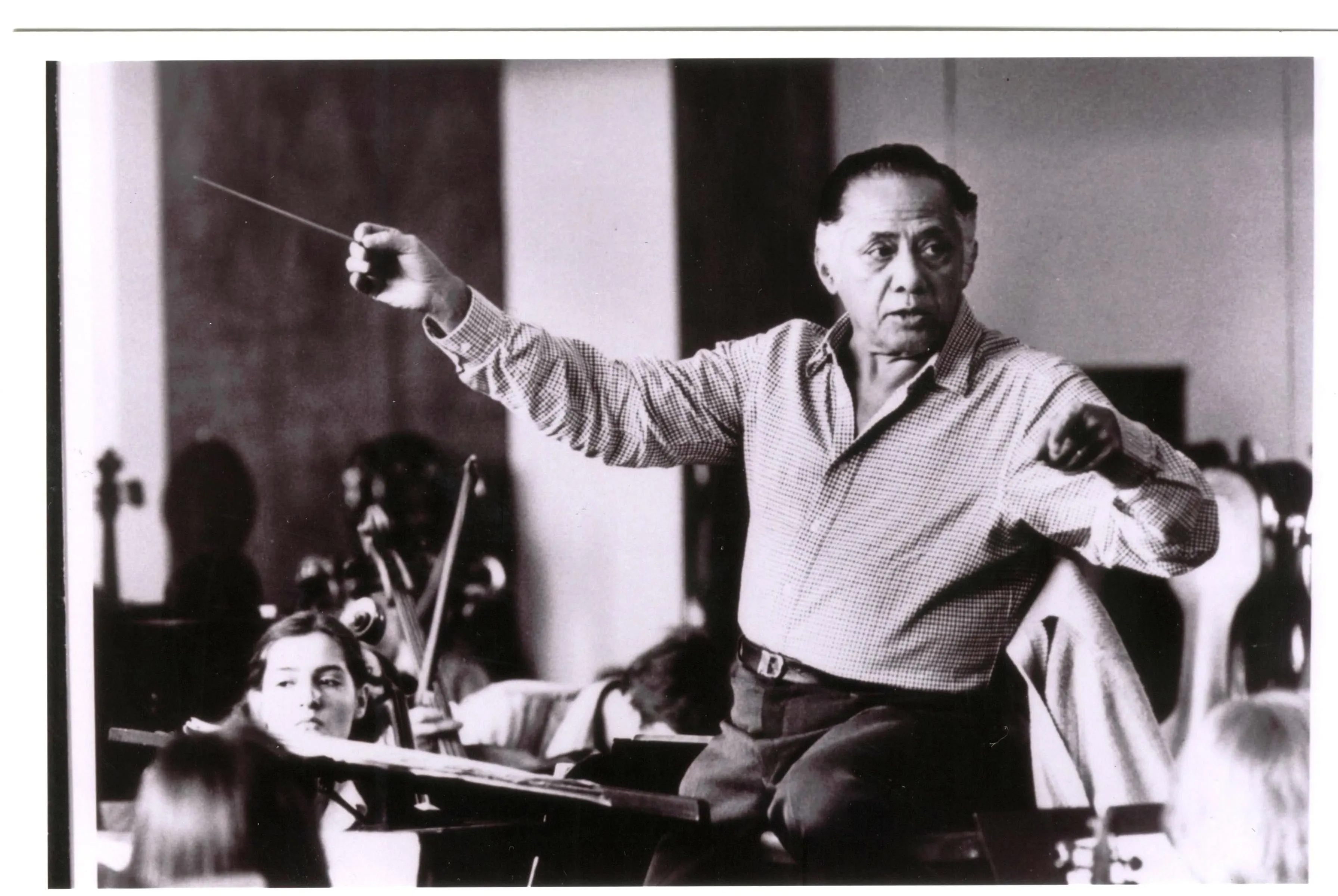 O maestro Eleazar de Carvalho é um homem de meia idade, branco. Ele veste uma camisa e segura a batuta com os braços abertos.