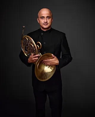 Luiz Garcia is a bald man with brown eyes. He is wearing black and holding a horn.