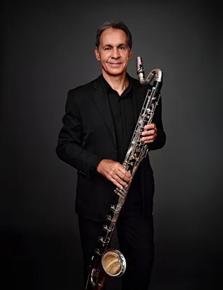 Nivaldo Orsi is a white man with gray hair, wearing a black shirt. He is holding a bass clarinet.