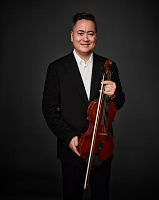 Peter Pas is an Asian man with black hair. He is wearing a white shirt and a black suit jacket, and he is holding a viola.