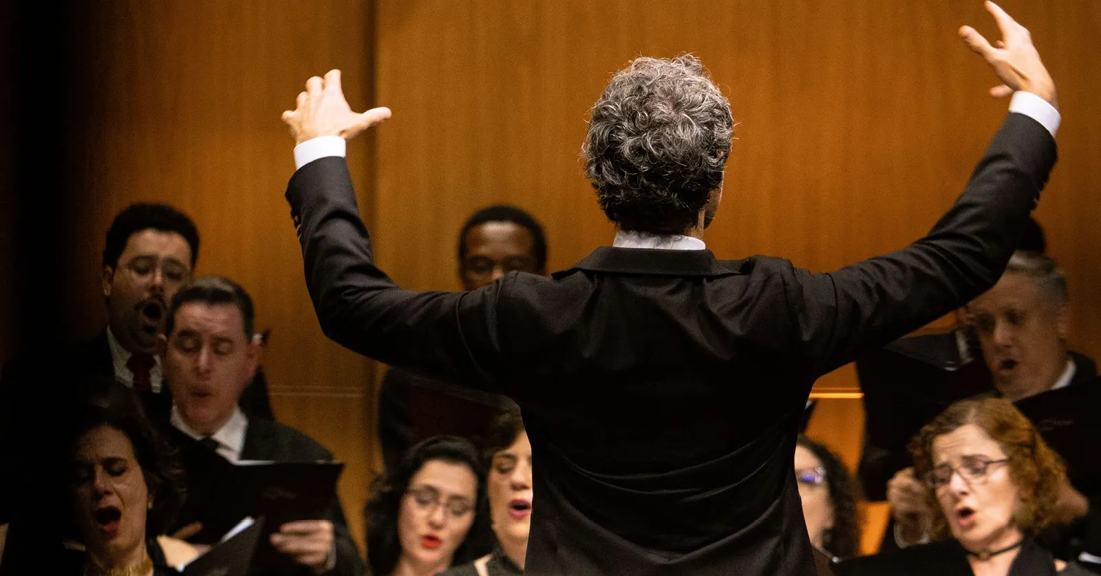Thomas Blunt está de costas com as mãos erguidas regendo o Coro.