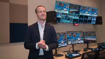 Foto do regente Christoph Koncz, homem branco, loiro, de cabelos curtos. Ele veste uma camisa social branca e um blazer escuro.