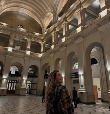 A imagem mostra uma mulher loira sorrindo na Sala São Paulo iluminada.