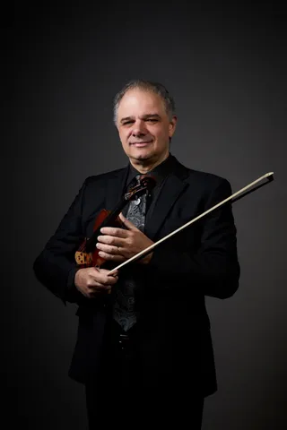 Igor Sarudiansky is a bald white man. He is holding a violin.