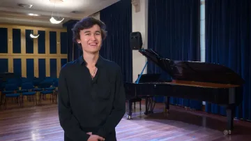Foto de Daniel Lozakovich. Homem branco de cabelos curtos e castanho. Usa camisa preta e blazer preto. Na foto, está sorrindo para a camera.
