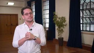 Foto de Flávio Lago, homem branco de cabelos castanhos e curtos. Ele veste camisa branca, usa óculos arredondados e um relógio no punho esquerdo.